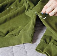 a person is sewing on the back of a green sweatshirt with white stitchs and thread