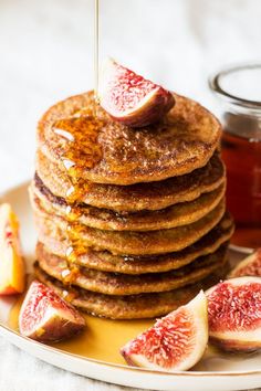 a stack of pancakes on a plate with sliced figs and honey being drizzled over them