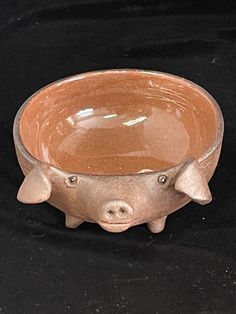 a small bowl with two little pigs on it's sides, sitting on a black surface