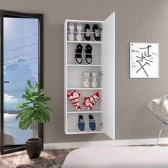 a white shelf with shoes on it next to a potted plant and a window