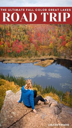 a woman sitting on top of a rock looking out over a lake and forest in the fall