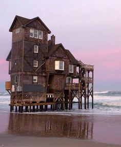 an old house on stilts in the ocean at sunset with waves crashing around it