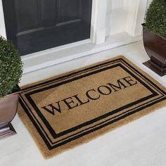 a welcome mat sitting on the ground next to two potted plants in front of a door