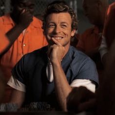 a smiling man sitting at a table with other men around him in orange shirts and ties