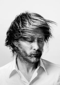 a black and white photo of a man with his hair blowing in the wind, looking down