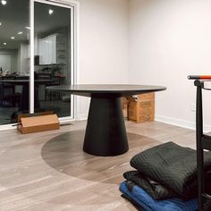 an empty room with a round table and black chair in it, next to other items on the floor