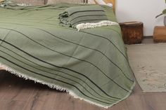 a bed covered in a green blanket on top of a wooden floor next to a plant