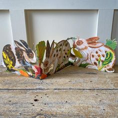 two paper rabbits sitting next to each other on top of a wooden table with leaves