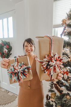 a woman holding two wrapped presents in front of a christmas tree