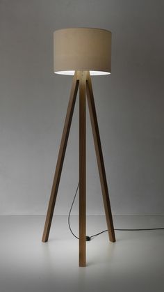 a wooden floor lamp with a beige shade on it's base and a cord plugged into the bulb