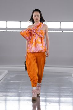 a model walks down the runway in an orange outfit with pink and yellow flowers on it