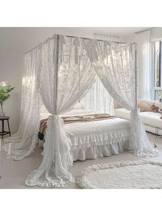 a white bed sitting in a bedroom next to a window with sheer curtains on it