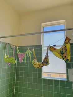 three bikinis hanging on a clothes line in a green tiled bathroom with a window