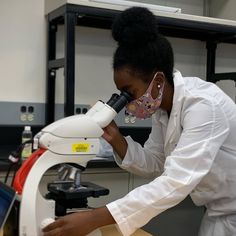 a woman looking through a microscope at something in front of her, while wearing a white lab coat