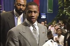 a man in a suit and tie standing next to another man with other people behind him