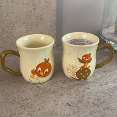 two coffee mugs with designs on them sitting on a counter top next to each other