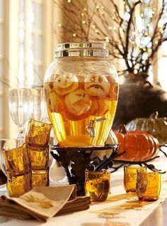 a pitcher filled with liquid sitting on top of a table next to glasses and pumpkins