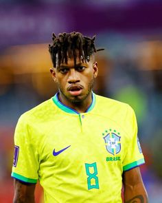 a soccer player with dreadlocks on his head looking at the camera while wearing a yellow shirt