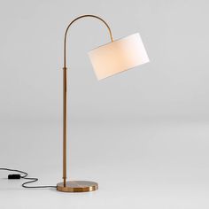 a floor lamp with a white shade on the base and a black cord plugged into it