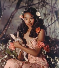 a woman holding a rabbit in her hands and flowers around her neck, sitting on the ground