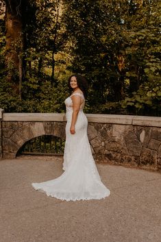 a woman in a wedding dress standing on a stone bridge with trees in the background