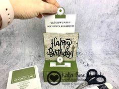 a hand holding a pair of scissors next to a birthday card and some other items
