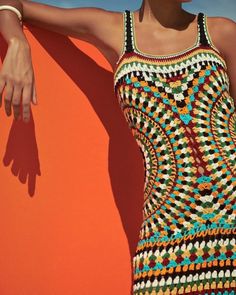 a woman in a crocheted dress leaning against an orange wall with her hand on the edge