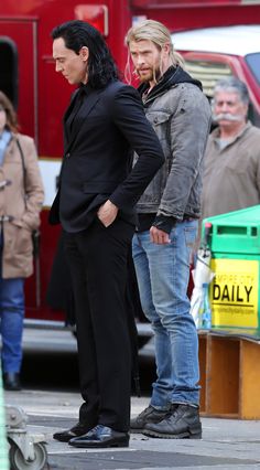 two men standing next to each other in front of a red fire truck on the street