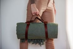 a woman holding a green duffel bag with brown straps on the bottom and tan pants