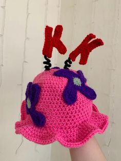 a crocheted pink hat with purple flowers on it and two red scissors sticking out of the top