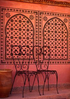 two wrought iron chairs sitting in front of a wall with an intricately designed design