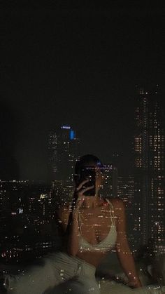 a woman sitting on top of a bed in front of a city skyline at night