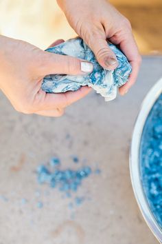 two hands are holding something in front of a bowl full of blue food and water