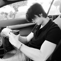 a man sitting in the back seat of a car holding a cup and looking at his cell phone