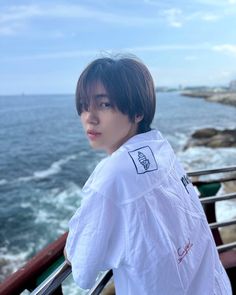 a young man standing on top of a balcony next to the ocean and looking at the camera