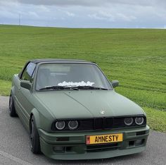 a green car parked on the side of a road in front of a grassy field