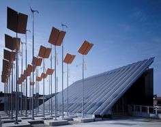 many flags are lined up in front of a building with a triangular design on the roof