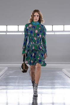 a model walks down the runway in a green dress with flowers on it and black boots