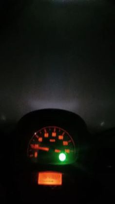 a car dashboard with the lights on and green light in the dark, as seen from behind