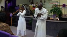 two people standing in front of a crowd with their hands on their chests and one person wearing a white dress