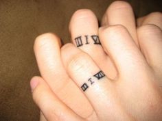 two fingers with roman numerals tattooed on them, one holding the other's hand