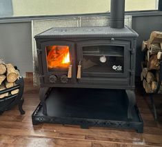 a wood burning stove sitting on top of a hard wood floor next to firewood