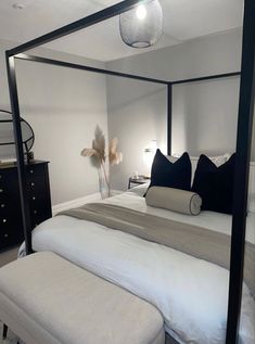 a bedroom with a four poster bed and white sheets, black pillows on the headboard