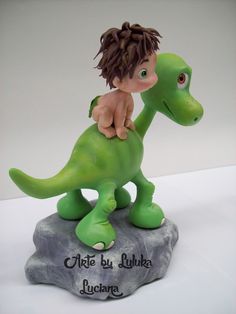 a little boy riding on the back of a green toy dinosaur that is sitting on top of a rock