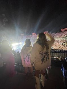 two women standing in the middle of a stadium at night with their hands on their head