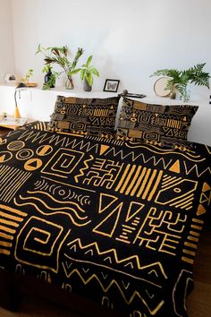 a bed covered in black and gold patterned comforter sets with plants on either side