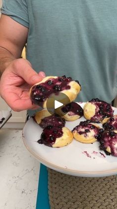 a man is holding a plate with blueberry donuts on it, and has one bite taken out