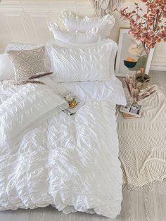 a bed with white comforter and pillows on it next to a vase filled with flowers