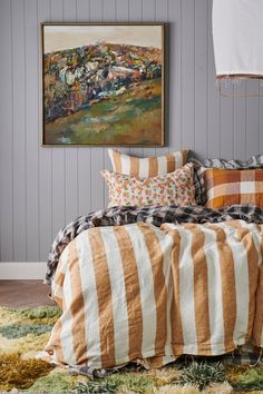 a bed with striped comforter and pillows on it next to a painting hanging over the headboard