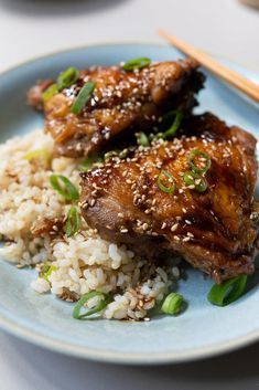 two pieces of meat on top of rice with chopsticks next to it in a blue plate